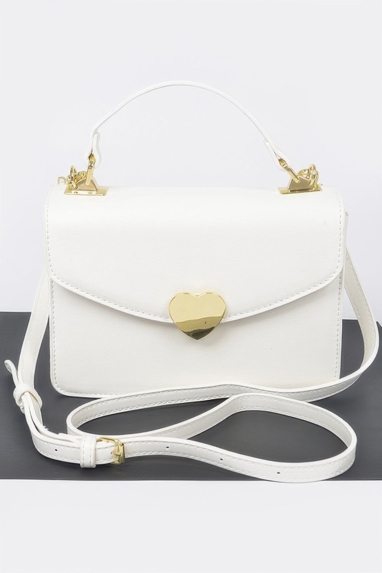 White crossbody bag with gold heart clasp and top handle, chic women's fashion accessory