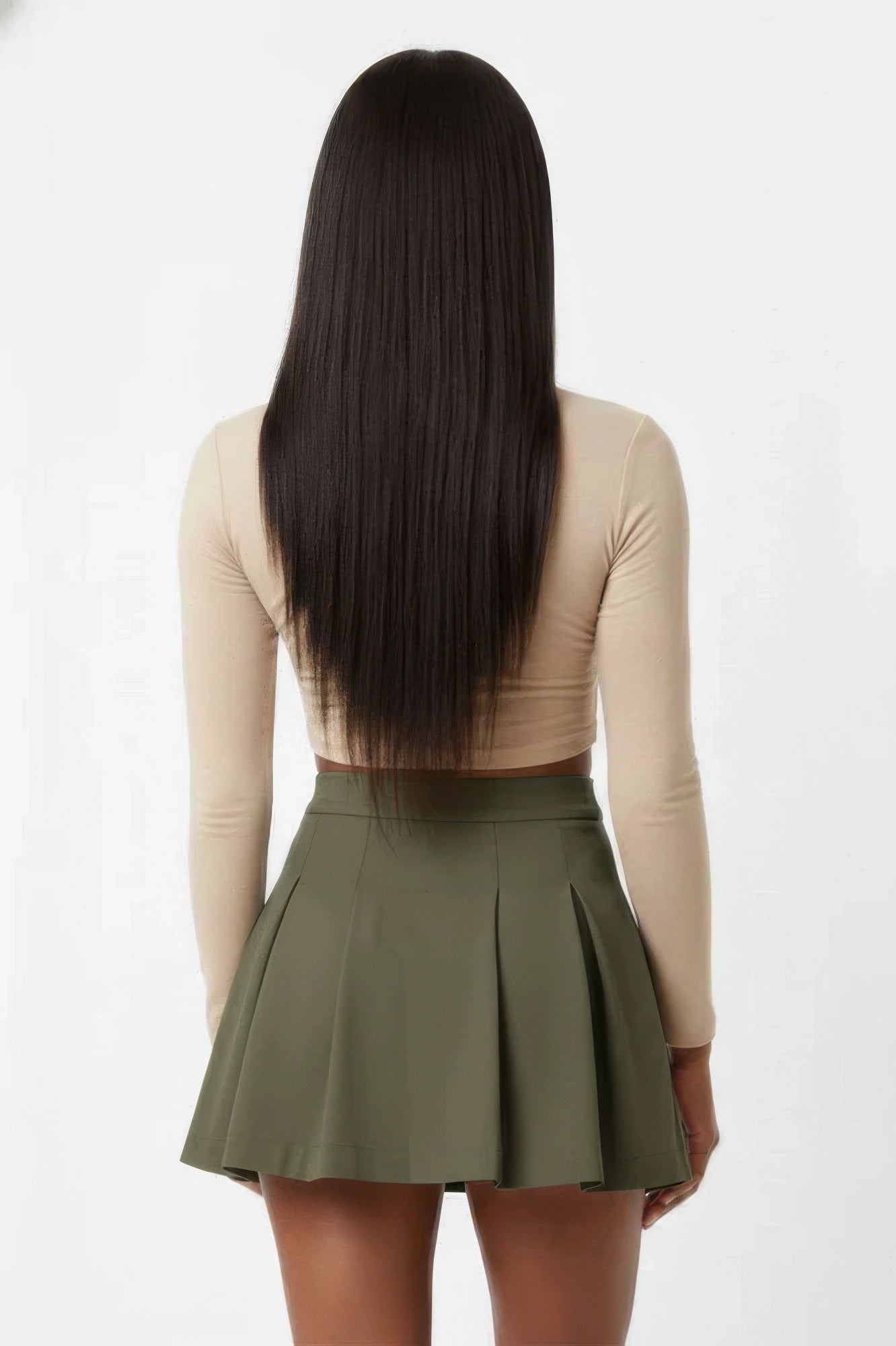 Woman wearing olive green pleated mini skirt with beige long sleeve crop top, back view