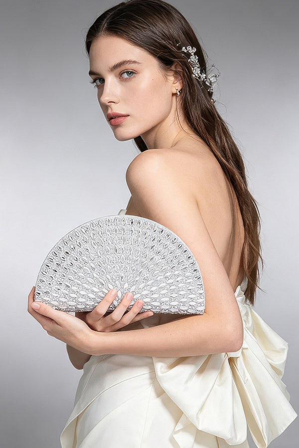 Elegant woman in white strapless dress holding silver lace clutch, styled with crystal hair accessory for formal events.