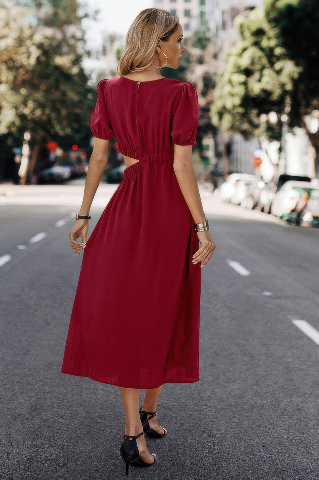 Woman in red midi dress with puff sleeves and back cutout, walking on city street