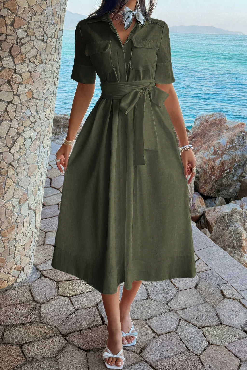 Olive green midi shirt dress with tie waist, pockets, and white sandals by the sea